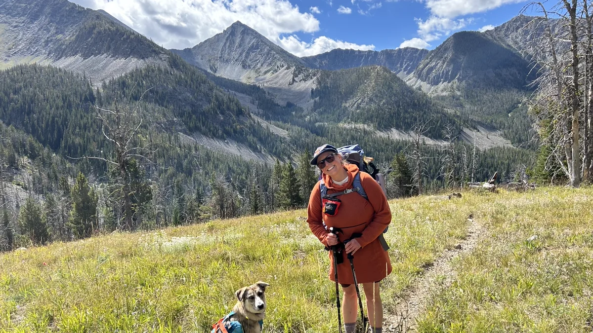 A hiker and dog on a controlled leash hiking along a mountain trail